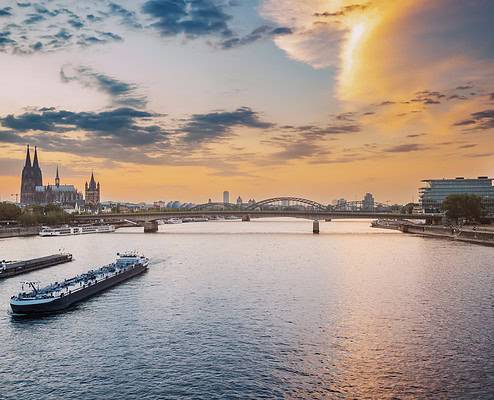 Date-Ideen in NRW: Stadtansicht der Stadt Köln, des Rheins, der Brücken und verschiedener Kähne und Schiffe während des Sonnenuntergangs.