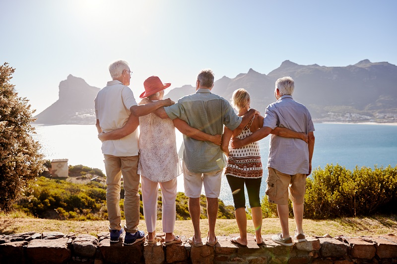 Rear View Of Senior Friends Visiting Tourist Landmark On Group Vacation Standing On Wall Singlereisen – Fernreisen